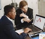 Two business professionals discuss marketing data on a laptop in a modern office.