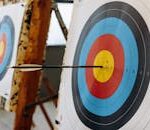 An arrow hits the bullseye on a colorful target in an indoor archery range.